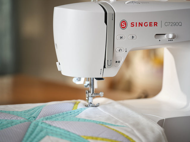 Close-up of the Singer C7290Q sewing machine quilting a fabric piece, featured in a comparison with the Brother CS600I.