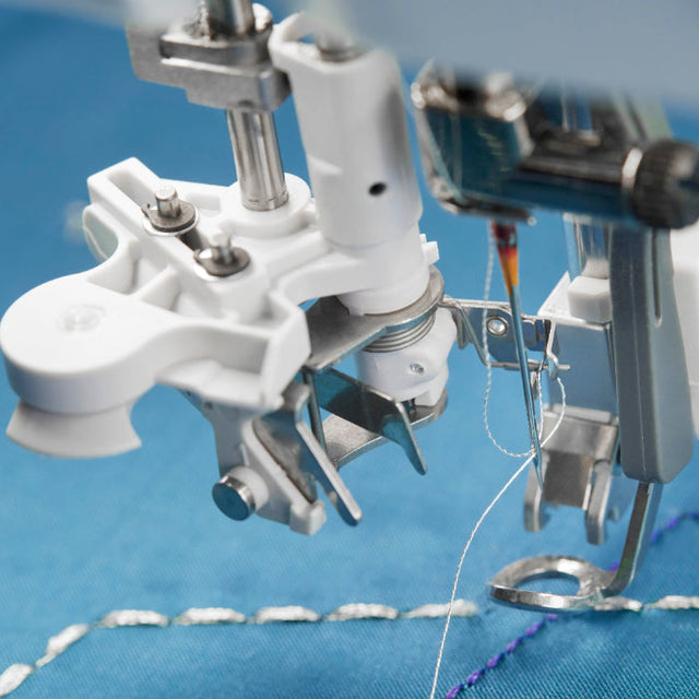 Close-up of a sewing machine needle and presser foot stitching blue fabric, with white and metallic components, ideal for quilting beginners learning machine techniques.